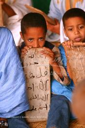 Image du Maroc Professionnelle de  Sous une tente on découvre la méthode traditionnelle de l’enseignement et l’apprentissage du saint coran prodigués aux enfants. Les jeunes récitent les sourates devant le Fkih (instituteur) qui écoute attentivement les versets ainsi récités, Samedi 18 septembre 2006, aux environ de Tan Tan dans un site désertique sur lequel la ville, a toujours accueilli la majorité des tribus et des grandes familles nomades du désert lors d'un grand Moussem, danses chants, course de chameaux et fantasia font partie des festivités. (Photo / Abdeljalil Bounhar)

